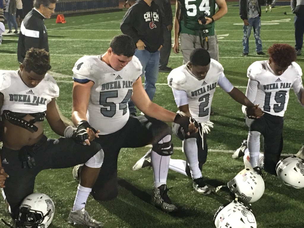 Buena Park players Ronnie Cannon, Ryan Nelson, Niguy Simms, and Jeremiah Hawkins kneel in prayer for teammate T'yon Johnson who broke his hand in the first quarter of the Coyotes, 42-0 victory over Warren.